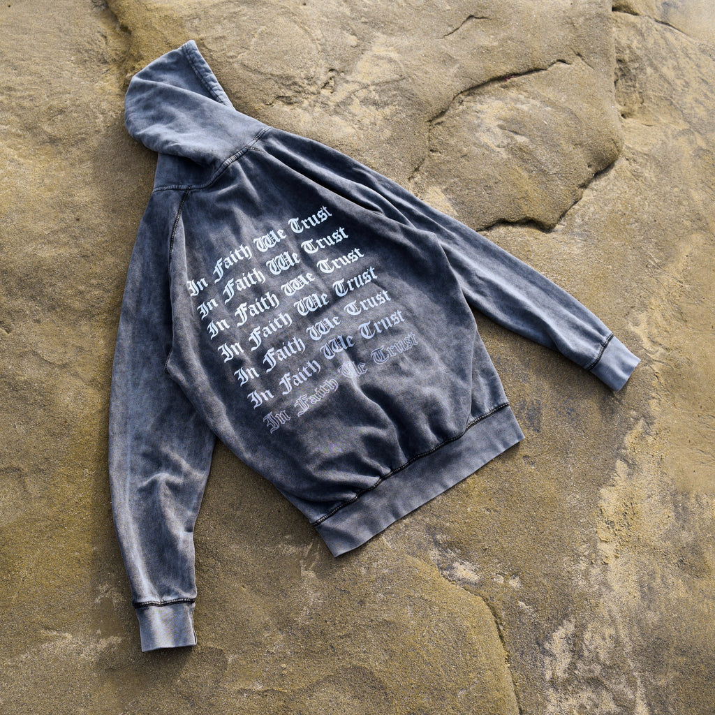 Back of In Faith We Trust Hoodie laying flat on a beach rock.
