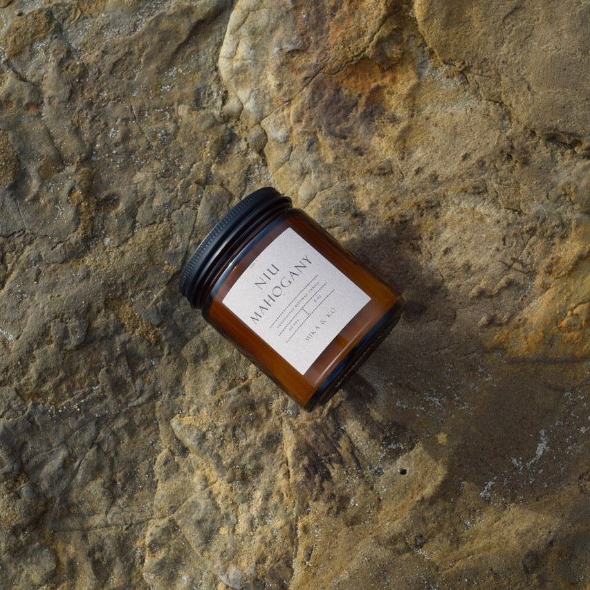 Niu Mahogany Candle photographed on a flat beach rock.