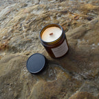 Niu Mahogany Candle open with the candle lid beside it photographed on a flat beach rock.